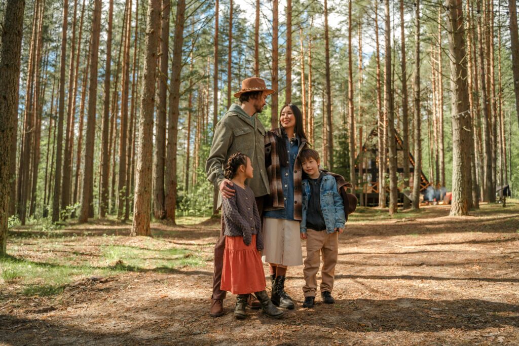 A family of four enjoys a peaceful vacation in a sunlit forest surrounded by tall pine trees.